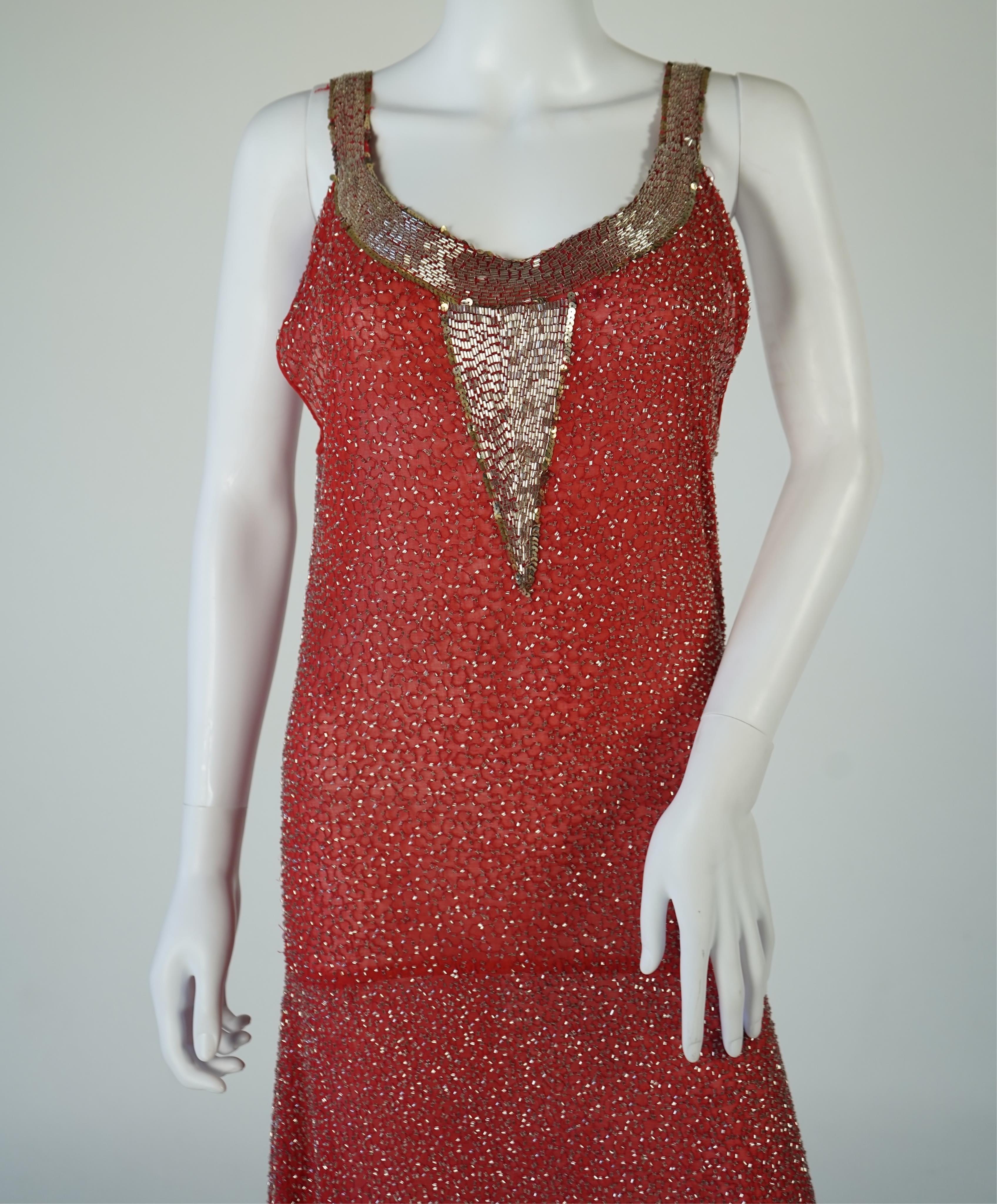 A 1920's red georgette beaded evening dress. Hand beaded and sequinned in white and gold, designed with a dropped waist, handkerchief points and wide beaded border with large stylistic floral motifs. Length 115cm. Condit